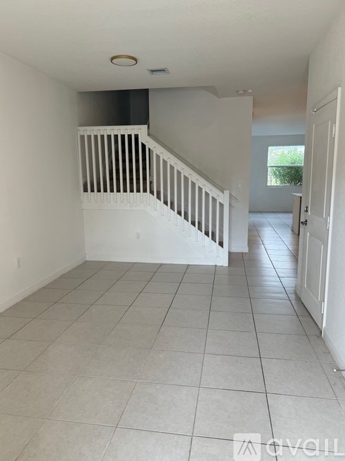 A white tiled hallway with a staircase and a door on the right.