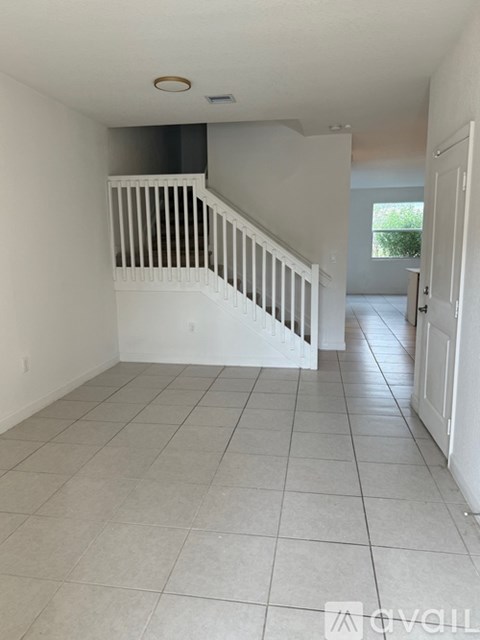 A white tiled hallway with a staircase and a door on the right.