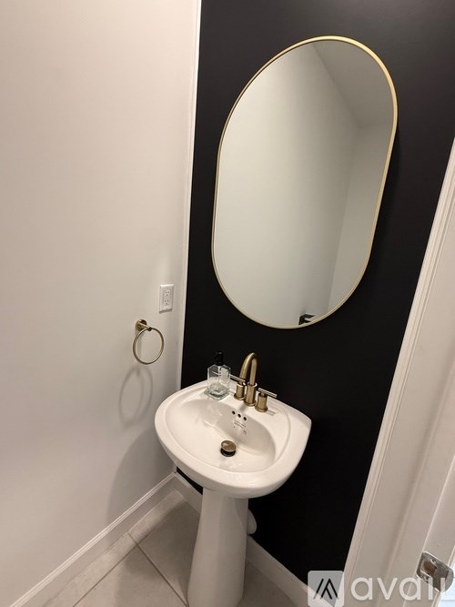 A white pedestal sink with a gold faucet and a round mirror above it.