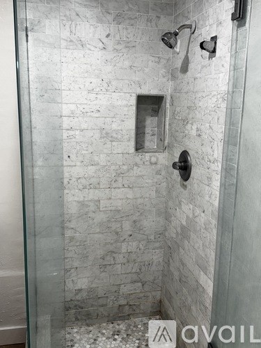 A shower with a glass door and a marble wall.