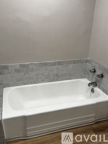 A white bathtub with a silver faucet is in a bathroom with a grey tiled wall.