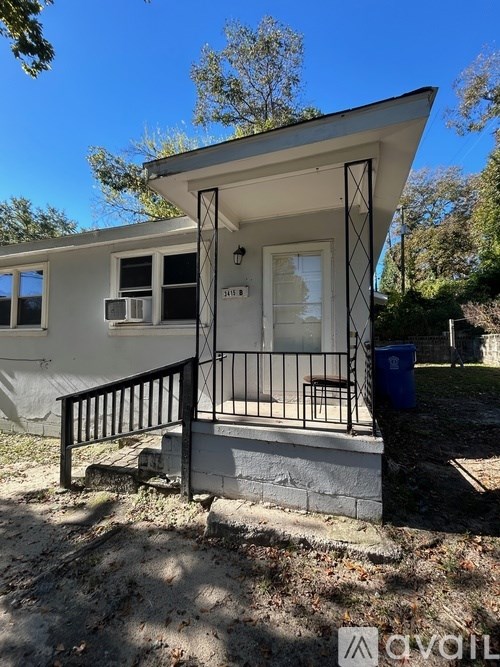 A small white house with a black railing and a blue trash can in front.