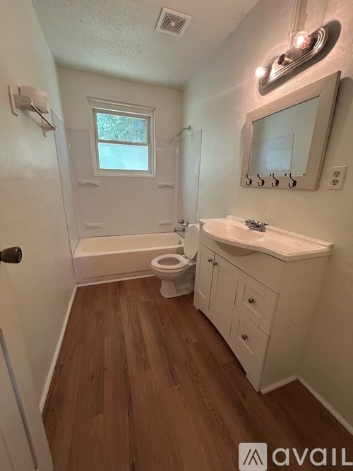A small white bathroom with wood floors and a window.