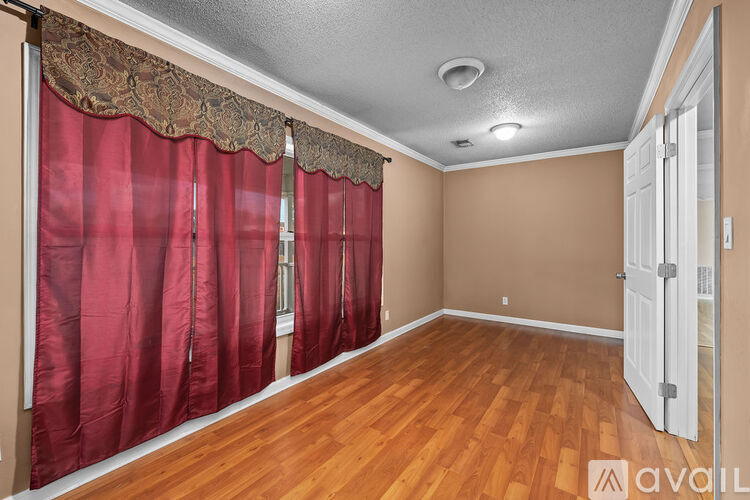 A spacious room with beige carpeting and walls, a door, and a window.