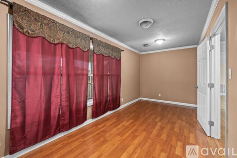 A spacious room with beige carpeting and walls, a door, and a window.