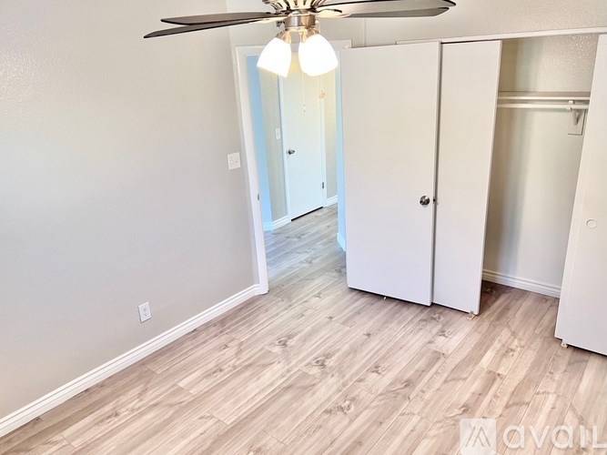 A room with a ceiling fan and light fixture, wooden flooring, and a white door.
