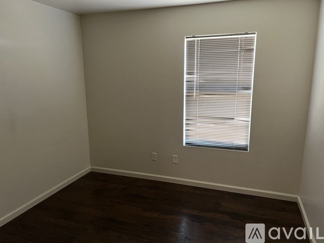 A room with a window covered by blinds and wooden flooring.