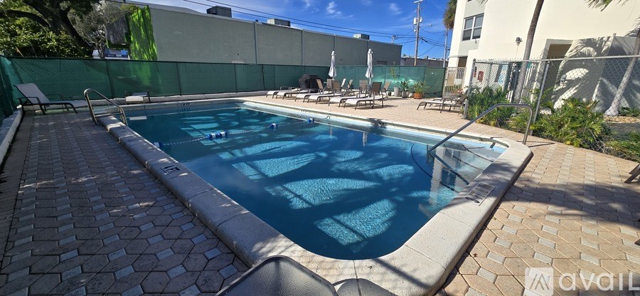 A pool surrounded by a brick patio and a green fence.