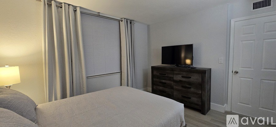 A bedroom with a bed, dresser, and window with curtains.