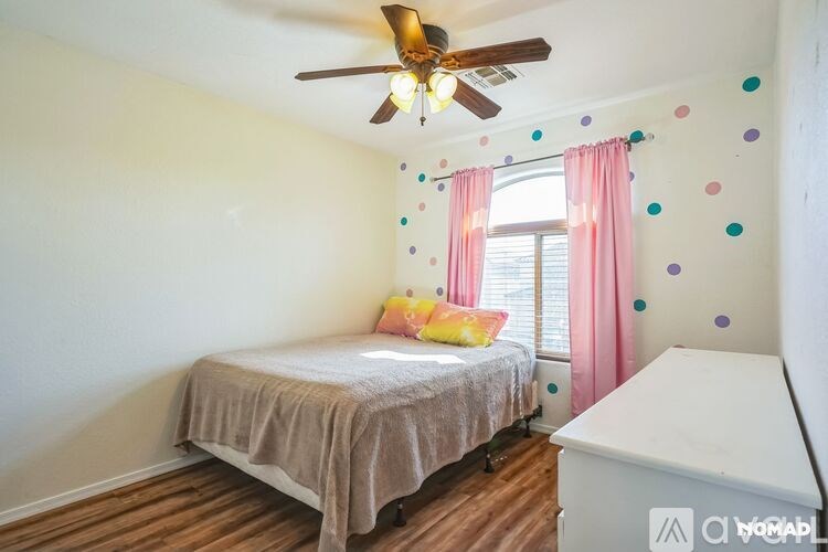 A bedroom with a bed, a ceiling fan, and a window with pink curtains.