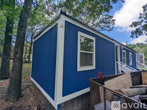 A blue and white cabin with a window and a door is surrounded by trees.
