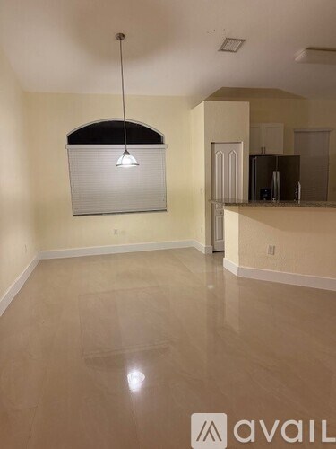 A room with a hanging light fixture and a kitchen area in the background.