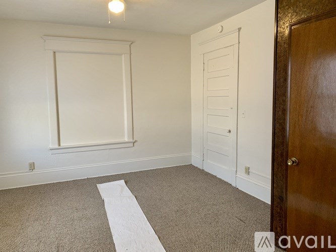 A room with a white door, a window with white trim, and a carpet with a white stripe down the middle.