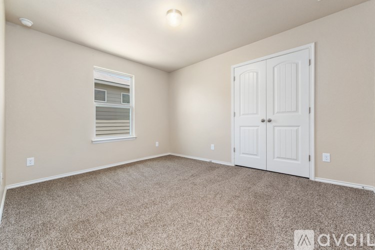 A room with a carpeted floor, a window with blinds, and a white door.