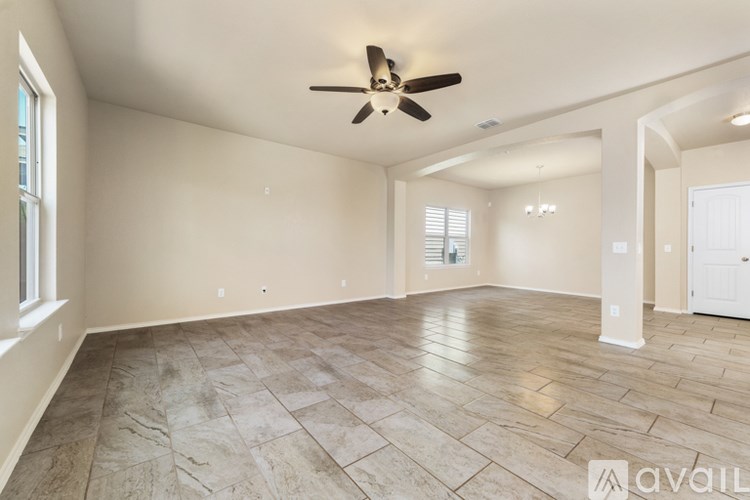 A spacious room with a ceiling fan and light, tile flooring, and a window with blinds.