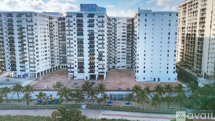 A large white building with a red roof is surrounded by other buildings and palm trees.