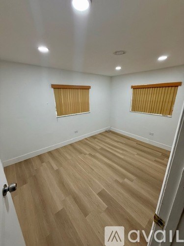 A room with wooden flooring and two windows with blinds.