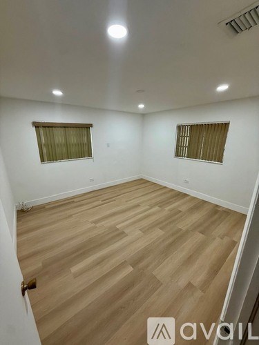 A room with wooden flooring and two windows with blinds.