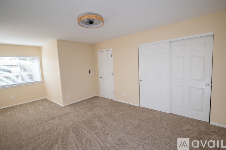 A room with a carpeted floor, two doors, and a window with blinds.
