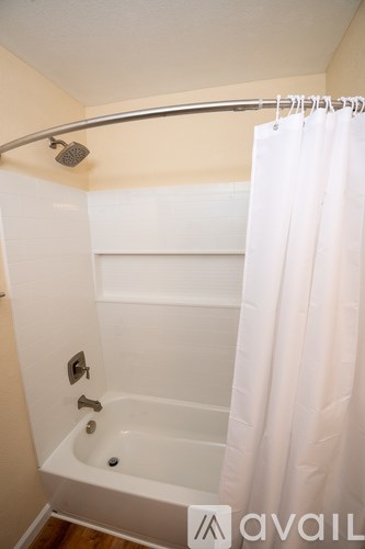 A white bathtub with a shower head and a white curtain.