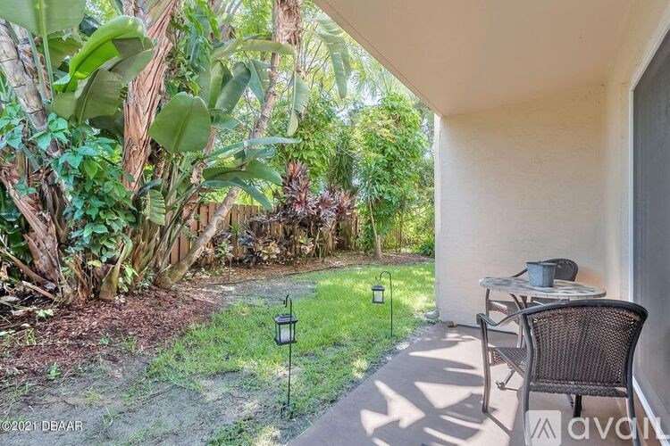 A patio with a chair and table is surrounded by greenery.