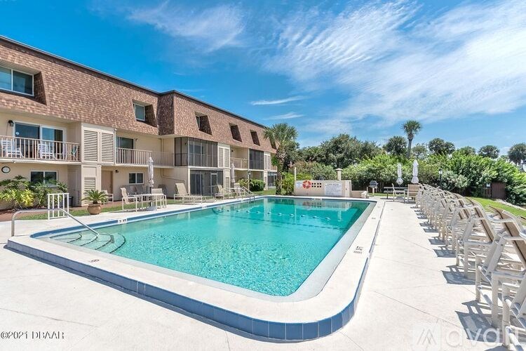 A large outdoor swimming pool surrounded by sun loungers and apartment buildings.
