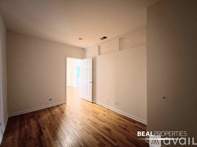 A room with wooden floors and white walls, with a doorway leading to another room.