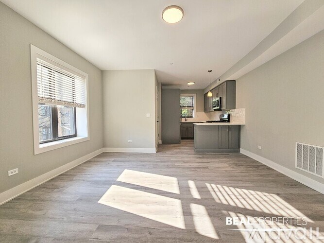 A spacious living room with a kitchen area in the background.