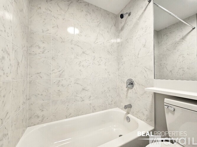 A white bathroom with a marble tile wall and a white bathtub.