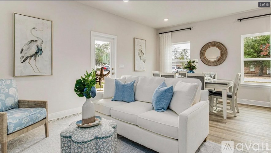 A living room with a white couch, a blue chair, and a white wall with a framed picture of a bird.