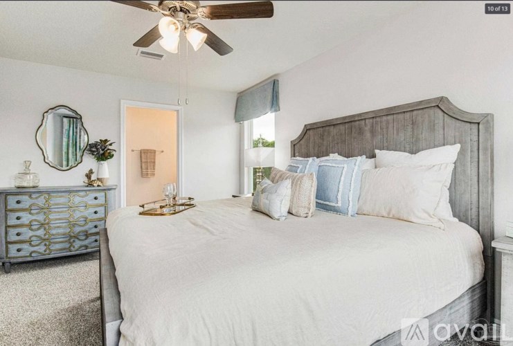 A bedroom with a large bed, a dresser with a mirror, and a ceiling fan.