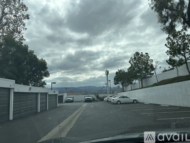 A cloudy day at the parking lot with cars parked and trees in the background.