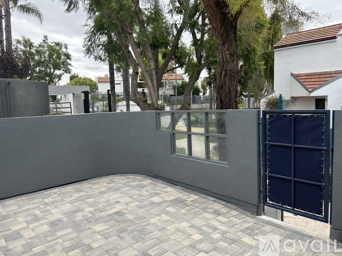 A grey fence surrounds a paved area with a tree in the background.