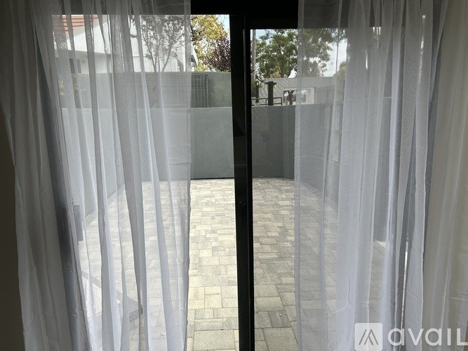 A view of a courtyard through a window with white curtains.