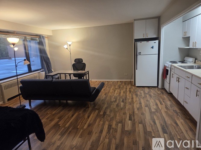 A living room with a black couch and a kitchen area with white cabinets.