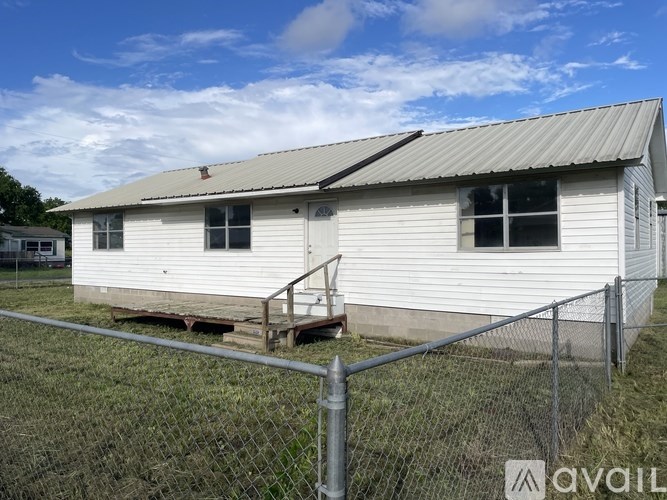 A white house with a metal roof and a fence in front.