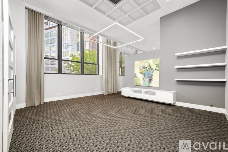 A spacious room with a carpeted floor, large windows, and a painting on the wall.