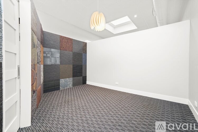A room with a grey carpet and a wall hanging with a white background.