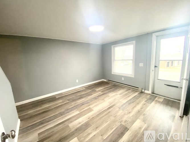 A room with wooden flooring and a door leading to a hallway.