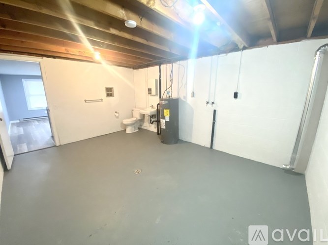 A spacious room with a concrete floor and white walls, featuring a window, a door, and a white cabinet.