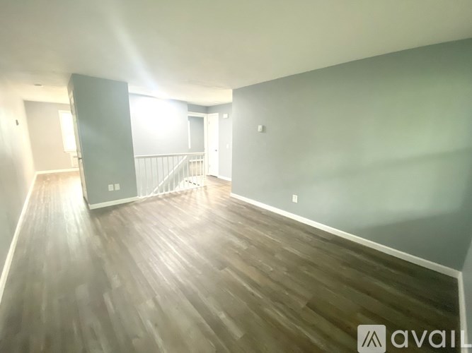 A spacious room with wooden flooring and a staircase in the background.