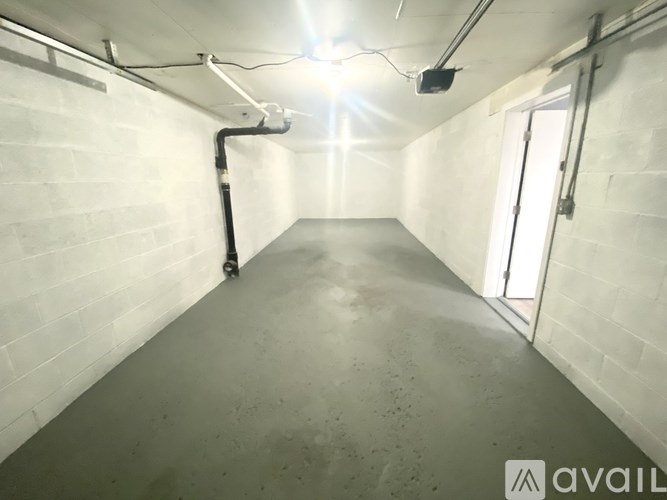 A long, narrow, concrete-floored room with white walls and a door on the right side.