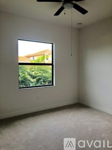 A room with a ceiling fan and a window overlooking a green area.