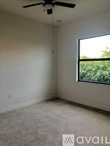 A room with a ceiling fan and a window overlooking greenery.