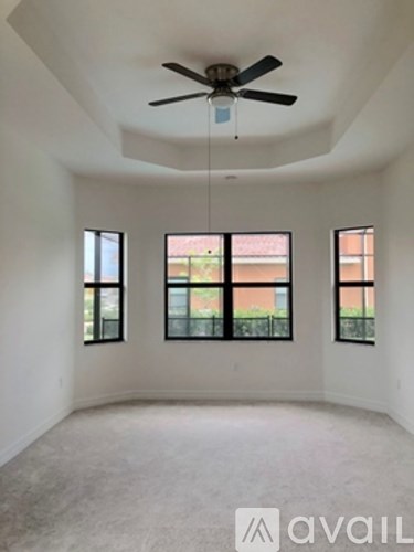 A room with a ceiling fan and three windows.