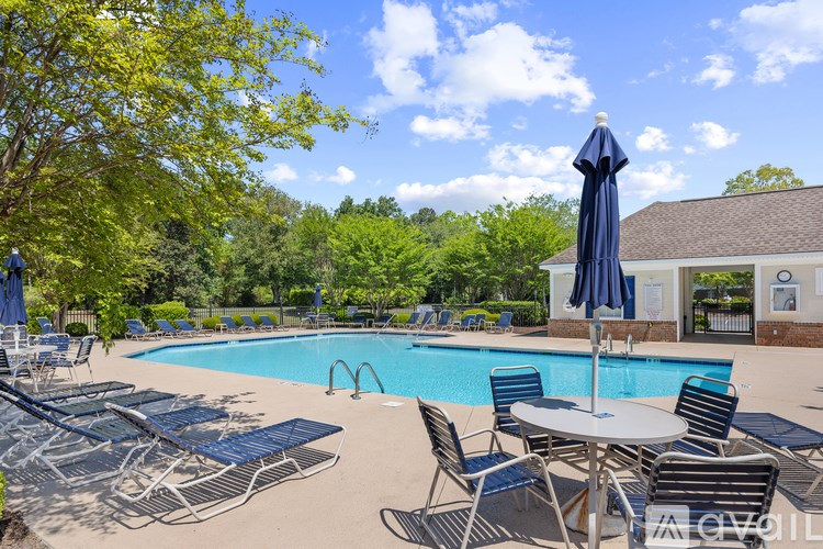 A pool area with chairs and umbrellas is surrounded by trees.