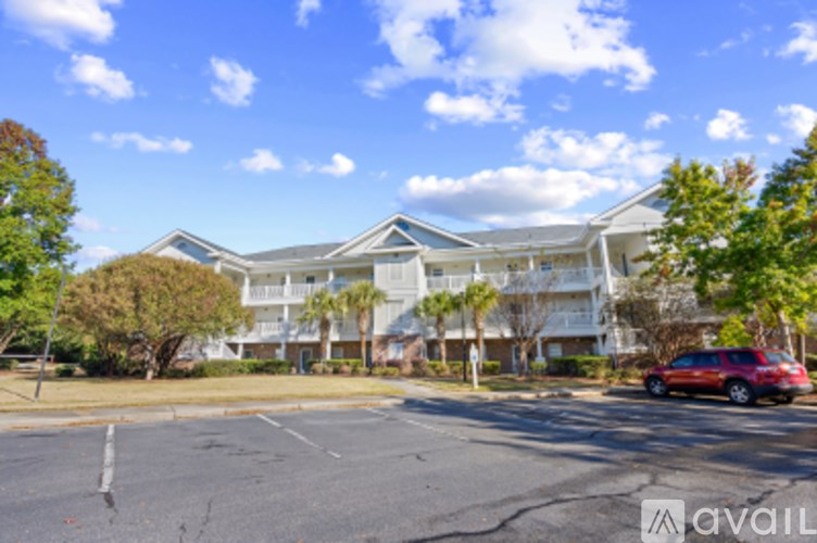 A red car is parked in a parking lot in front of a white building.