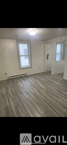 A room with wooden flooring and two windows.