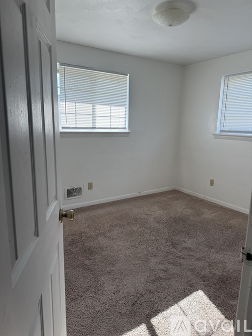 A room with a carpeted floor and two windows with blinds.