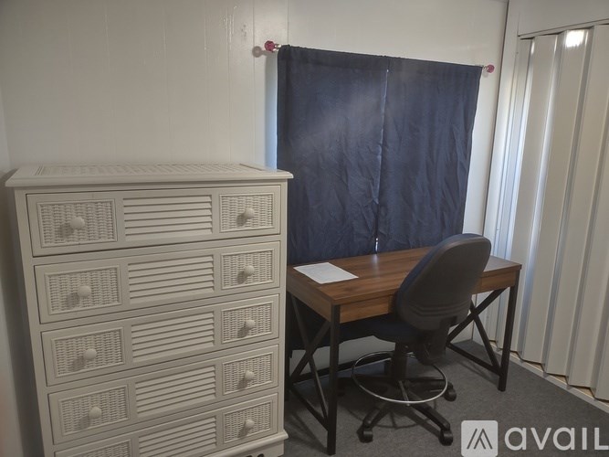 A white cabinet with drawers is next to a desk with a chair.